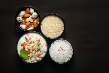 Close-up of Creamy rice Kheer(khir) Garnished with basil leaf, saffron and dry fruits. Indian delicious dessert. Served in a ceramic black bowl. Top View on black background.