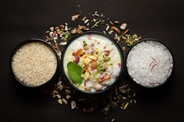 Close-up of Creamy rice Kheer(khir) Garnished with basil leaf, saffron and dry fruits. Indian delicious dessert. Served in a ceramic black bowl. Top View on black background.