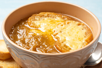Traditional french onion soup with baguette and cheese in bowl on concrete background