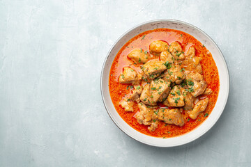 Chicken stew with paprika, onion and sour cream in plate on concrete background. Traditional Hungarian dish Paprikash.