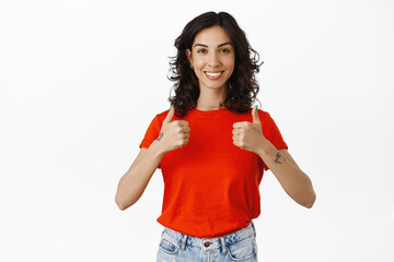 Well done, yes. Smiling satisfied brunette girl shows thumbs up, like and agrees, approves...