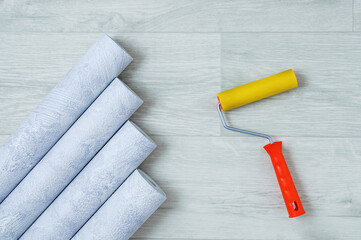 Gray textured wallpaper rolls and wallpaper roller on  white wooden background.