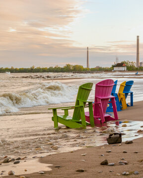 Toronto Beaches sunset with waves breaking on the sand and colorful plastic muskoka chairs in the surf, seen from Kew Beach in Toronto's east end.