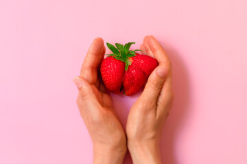 Above view of woman hands holding ugly funny strawberry on pastel pink background. Ugly food concept