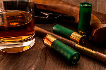 Hunting rifle and 12 gauge bullets with glass of whiskey and a ramrod for cleaning weapons lying on...