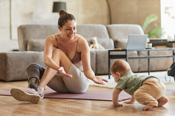 Full length portrait of active mother with disability playing with cute baby while sitting on floor at home, copy space - obrazy, fototapety, plakaty