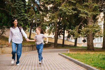 Obraz premium A little girl with her mother runs along the sidewalk in the park. Active play in nature.