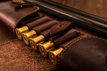 Hunting ammunition 12 gauge in leather bandolier and double-barreled shotgun on a wooden table....