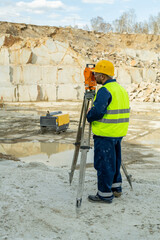 Young surveyor in workwear using geodetic station on construction place
