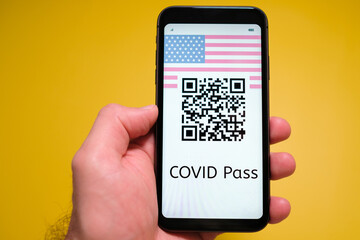 Covid pass with QR code with USA flag on the screen in smartphone in mans hand on the yellow background, May 2021, San Francisco, USA.