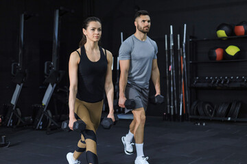 Attractive sports people are working out with dumbbells at gym.