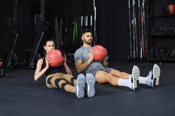 Fit and muscular couple exercising with medicine ball at gym.