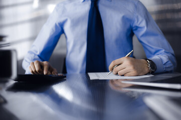 Unknown man accountant in blue shirt use calculator and computer with holding pen on while staying...