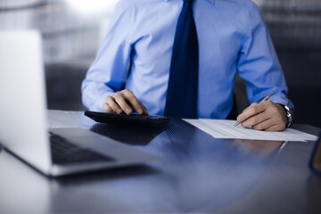 Unknown man accountant in blue shirt use calculator and computer with holding pen on while staying...