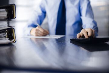 Unknown man accountant in blue shirt use calculator and computer with holding pen on while staying...