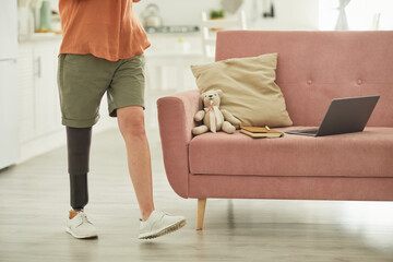 Low section portrait of modern woman with leg prosthesis walking across room in minimal home interior, copy space