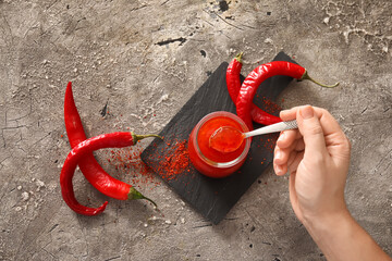 Woman holding spoon with tasty chili sauce on grunge background