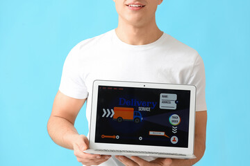 Young man and laptop with open page of delivery service application on color background
