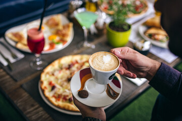 man holding cup of coffee in front of pizza in restaurant