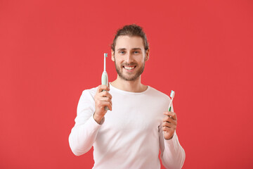 Handsome man with tooth brushes on color background