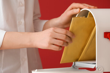 Woman getting letter from box on color background