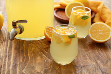 Jar and glasses of tasty cold lemonade on wooden background