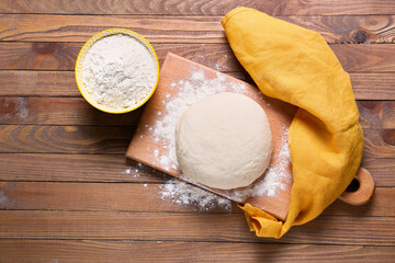 Board with fresh dough and flour on wooden background