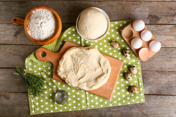 Composition with fresh dough, flour, eggs and rosemary on wooden background