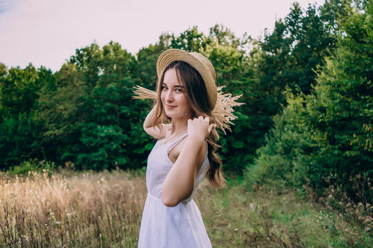 Young woman in a straw hat on a background of tall herbs. Beautiful girl in a dress with a bouquet of dried flowers in the field.