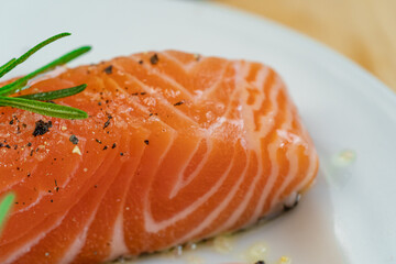 Salmon steak a piece of fresh home cooking with rosemary, olive oil, black pepper and himalayan salt on a white plate. Focus select and blur close up and Macro photography.