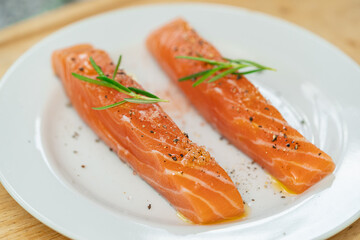 Salmon steak a piece of fresh home cooking with rosemary, olive oil, black pepper and himalayan salt on a white plate. Focus select and blur close up and Macro photography.