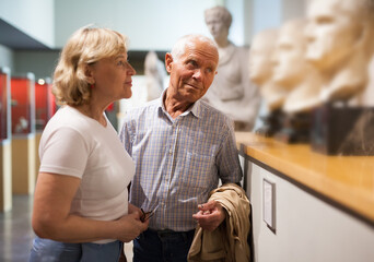 Positive elderly couple looking at exhibits on exposition of museum