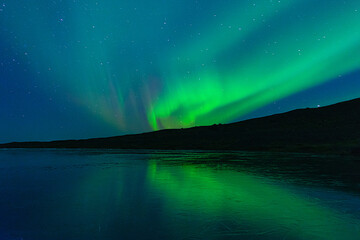 Northern Lights on the night sky. Wintertime starry sky. Aurora Borealis above a frozen lake.