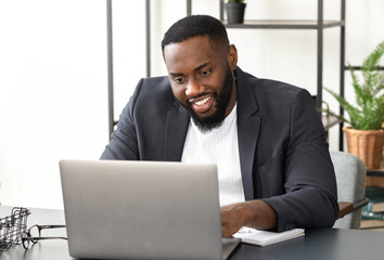 Successful young African American businessman using laptop for video communication with employees....