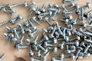 A lot of metal self-tapping screws are scattered on wooden background. Short fix for aluminum and metal. Silver color. Hardware product store. Cross on the head. Fastening material. Construction tool