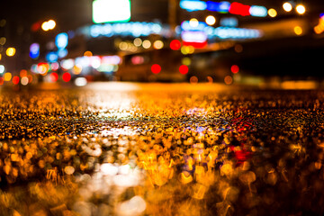 Rainy night in the big city, light from the shop windows reflected on the road. View from the level of asphalt