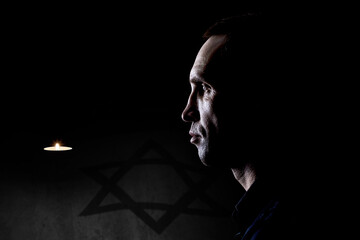 A man near a burning candle on the background of the flag of Israel. Holocaust Memorial Day.