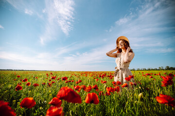Young woman walking in amazing poppy field. Summertime. Beautiful woman posing in the blooming...