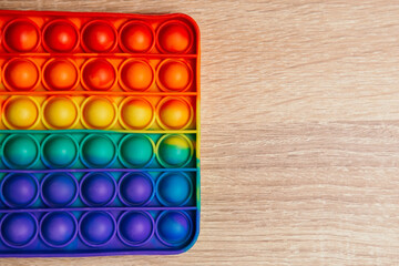 Simple dimple colorful anti stress pop it on wooden table. Fidget trendy rubber kids children toy neuropathy fight nerves for playing having fun. Copy space. Rainbow finger gadget. Silicone