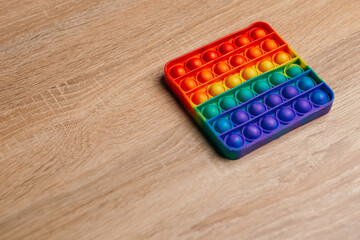 Simple dimple colorful anti stress pop it on wooden table. Fidget trendy rubber kids children toy neuropathy fight nerves for playing having fun. Copy space. Rainbow finger gadget. Silicone