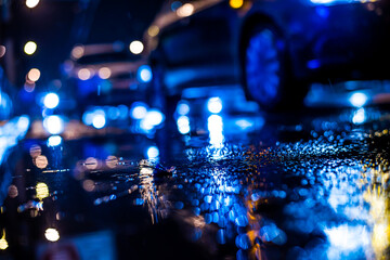 Fototapeta na wymiar Rainy night in the big city, approaching headlights of cars traveling along the avenue. View from the level of the curb on the road