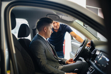 A young businessman with a salesman looks at a new car in a car dealership. Buying a car