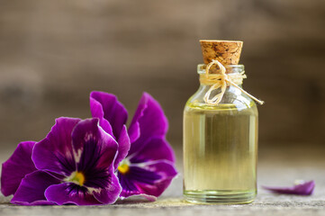Obraz na płótnie Canvas Glass bottle of essential pansy oil with fresh violet flowers, beauty treatment, alternative medicine