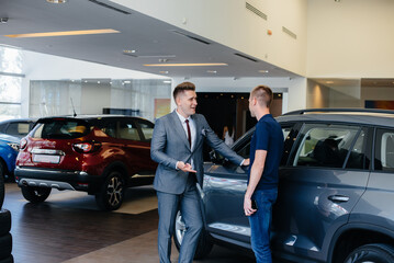 Fototapeta na wymiar A young businessman with a salesman looks at a new car in a car dealership. Buying a car