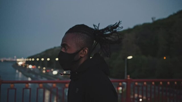 Close up portrait of spoty african american guy wearing protective face mask running on public city bridge in evening