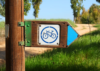 Wooden signpost with a bicycle symbol indicating the moving direction for cyclists along a trail in...