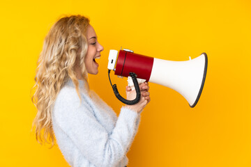 Young blonde woman isolated on yellow background shouting through a megaphone