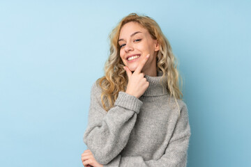 Young blonde woman wearing a sweater isolated on blue background smiling