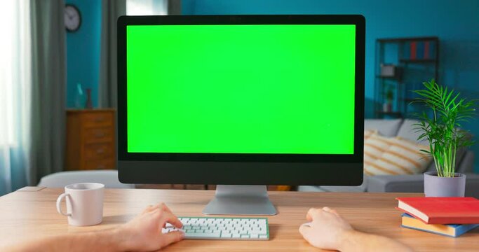 Shot of Male Hands Typing on a keyboard computer with blank screen. Modern Personal Computer with Mock-up Green Screen Display Standing on the Desk of the Cozy Home