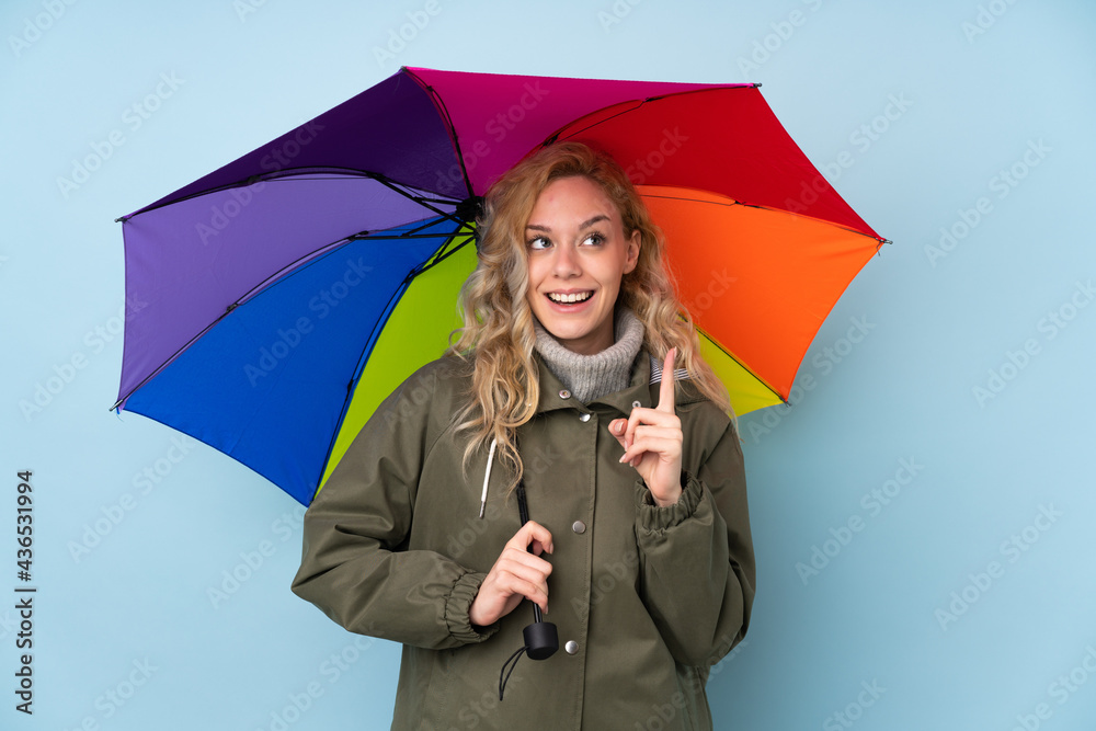 Canvas Prints Young blonde woman holding an umbrella isolated on blue background intending to realizes the solution while lifting a finger up